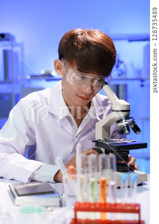 Young scientist looking through a microscope in the laboratory. 128735489