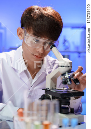 Young scientist looking through a microscope in the laboratory. Young scientist looking through a microscope in the laboratory. 128735490
