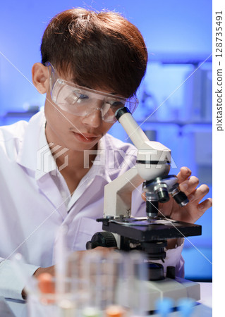 Young scientist looking through a microscope in the laboratory. Young scientist looking through a microscope in the laboratory. 128735491