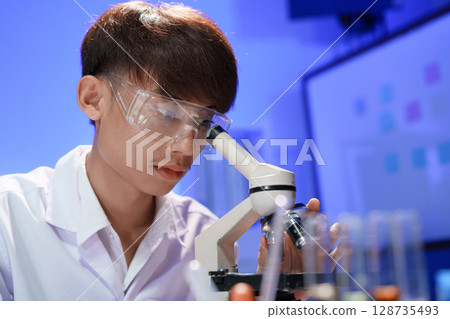 Young scientist looking through a microscope in the laboratory. Young scientist looking through a microscope in the laboratory. 128735493