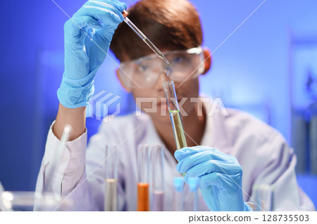 Scientists working in Laboratory using pipette dropping liquid sample into test tube. 128735503