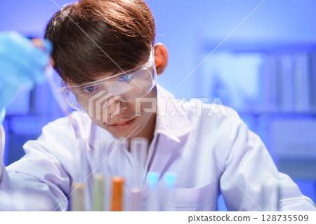 Scientists working in Laboratory using pipette dropping liquid sample into test tube. Scientists working in Laboratory using pipette dropping liquid sample into test tube. 128735509