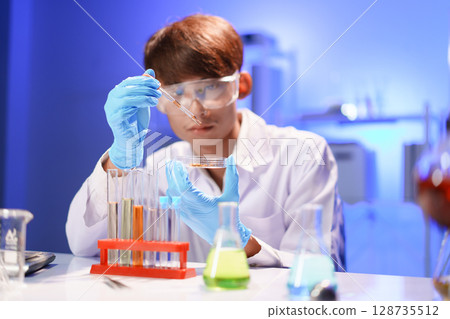Female lab technician holding pipette above Petri dish. Young scientist doing analysis in the laboratory. 128735512