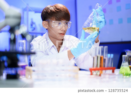A young male scientist examining a in beaker a lab. 128735524