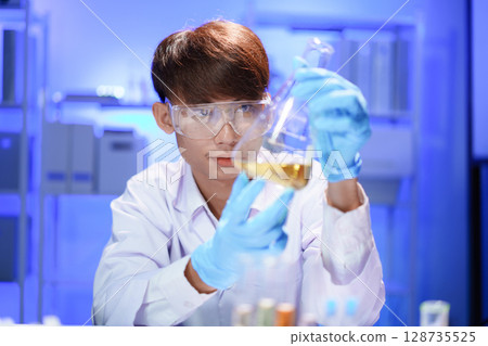 A young male scientist examining a in beaker a lab. 128735525