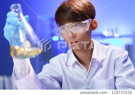 A young male scientist examining a in beaker a lab. 128735526