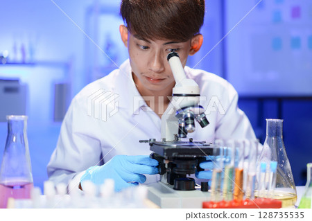 Young scientist looking through a microscope in the laboratory. Young scientist looking through a microscope in the laboratory. 128735535