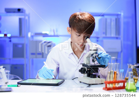 Young scientist looking through a microscope in the laboratory. Young scientist looking through a microscope in the laboratory. 128735544