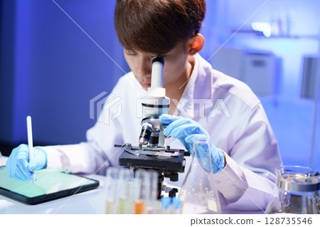 Young scientist looking through a microscope in the laboratory. Young scientist looking through a microscope in the laboratory. 128735546