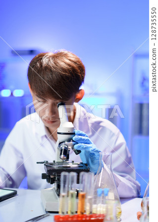 Young scientist looking through a microscope in the laboratory. Young scientist looking through a microscope in the laboratory. 128735550