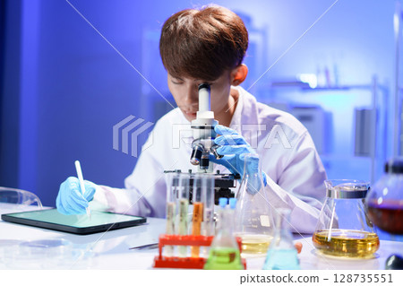 Young scientist looking through a microscope in the laboratory. 128735551