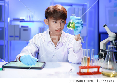 A young male scientist examining a in beaker a lab. 128735555