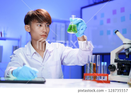 A young male scientist examining a in beaker a lab. 128735557