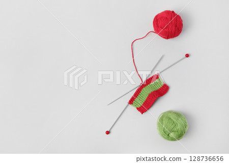 Red knitted wool on gray background with knitting needles for knitting warm clothes and hobbies needlework. Knitting a striped Christmas scarf with red and green threads 128736656