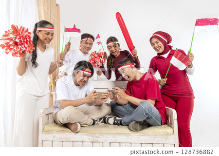 Portrait of an Indonesian southeast asian people celebrating Indonesia Independence Day on the 17th of August with a game of playing video games on cellphone at home. Concept of Kemerdekaan Indonesia Portrait of an Indonesian southeast asian people celebrating Indonesia Independence Day on the 17th of August with a game of playing video games on cellphone at home. Concept of Kemerdekaan Indonesia 128736882