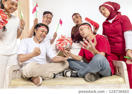 Portrait of an Indonesian southeast asian people celebrating Indonesia Independence Day on the 17th of August with a game of playing video games on cellphone at home. Concept of Kemerdekaan Indonesia 128736883