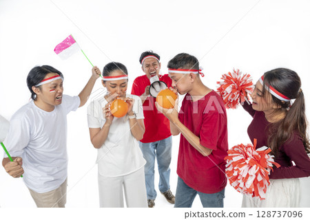 Portrait of an Indonesian southeast asian people celebrate Indonesia Independence Day on 17th of August with a game of blowing balloons isolated over white background. Concept of Kemerdekaan Indonesia 128737096