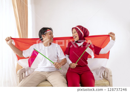 Portrait of an Indonesian southeast asian people celebrating Indonesia Independence Day on the 17th of August by holding the Indonesian national flag at home. Concept of Kemerdekaan Indonesia Portrait of an Indonesian southeast asian people celebrating Indonesia Independence Day on the 17th of August by holding the Indonesian national flag at home. Concept of Kemerdekaan Indonesia 128737246