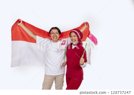 Indonesian southeast asian people celebrating Indonesia Independence Day on the 17th of August by holding the Indonesian national flag isolated over white background. Concept of Kemerdekaan Indonesia Indonesian southeast asian people celebrating Indonesia Independence Day on the 17th of August by holding the Indonesian national flag isolated over white background. Concept of Kemerdekaan Indonesia 128737247