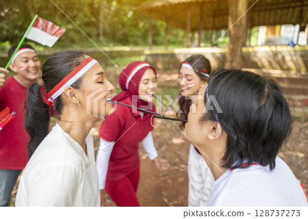 Portrait of an Indonesian southeast asian people celebrate Indonesia Independence Day on the 17th of August with a game of moving the rubber band with a straw outdoors. Concept of Kemerdekaan 128737273