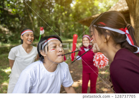 Portrait of an Indonesian southeast asian people celebrate Indonesia Independence Day on the 17th of August with a game of moving the rubber band with a straw outdoors. Concept of Kemerdekaan 128737705