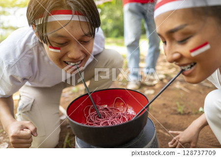 Portrait of an Indonesian southeast asian people celebrate Indonesia Independence Day on the 17th of August with a game of moving the rubber band with a straw outdoors. Concept of Kemerdekaan 128737709