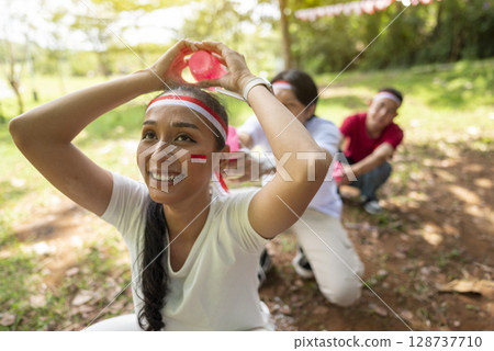 Portrait of an Indonesian southeast asian people celebrate Indonesia Independence Day on the 17th of August with a game of moving flour with plastic glasses outdoors. Concept of Kemerdekaan Indonesia 128737710
