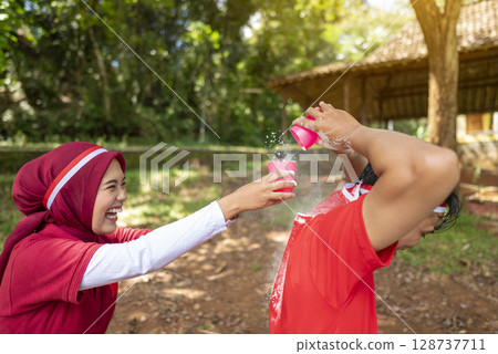 Portrait of an Indonesian southeast asian people celebrate Indonesia Independence Day on the 17th of August with a game of moving flour with plastic glasses outdoors. Concept of Kemerdekaan Indonesia 128737711