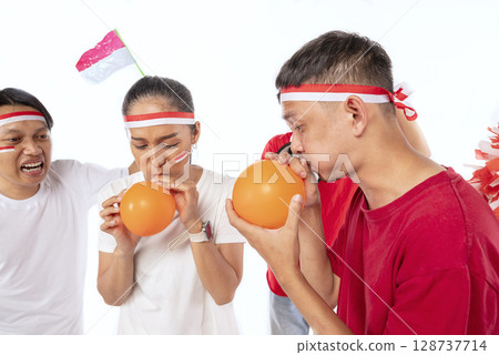 Portrait of an Indonesian southeast asian people celebrate Indonesia Independence Day on 17th of August with a game of blowing balloons isolated over white background. Concept of Kemerdekaan Indonesia Portrait of an Indonesian southeast asian people celebrate Indonesia Independence Day on 17th of August with a game of blowing balloons isolated over white background. Concept of Kemerdekaan Indonesia 128737714