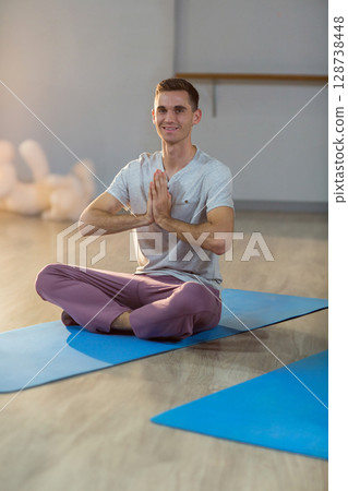 Young adult male practicing meditation on yoga mat in bright yoga studio with serene focus Young adult male practicing meditation on yoga mat in bright yoga studio with serene focus 128738448