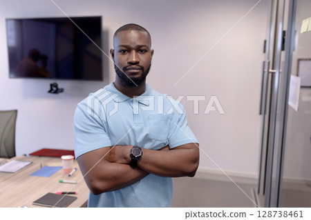 Young African American man standing with crossed arms in modern office, wearing watch, copy space Young African American man standing with crossed arms in modern office, wearing watch, copy space 128738461