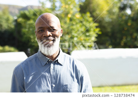 Senior African American man standing in garden, wearing light blue button-down shirt, smiling 128738474
