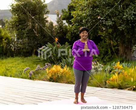 Senior mixed woman practicing yoga on pink yoga mat in outdoor garden, exuding calm energy Senior mixed woman practicing yoga on pink yoga mat in outdoor garden, exuding calm energy 128738475