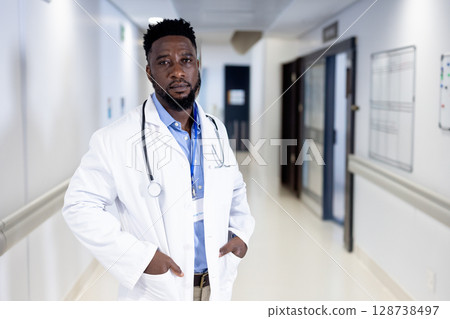 Mid adult African American man standing in hospital corridor, with stethoscope and ID badge visible 128738497