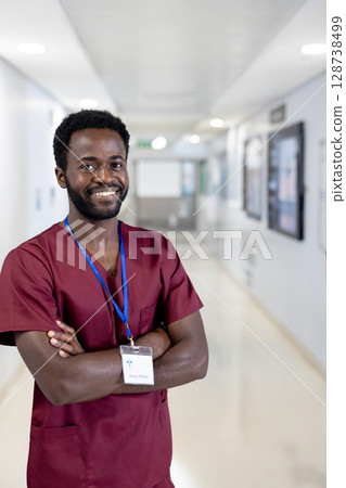 Young African American man standing in hospital corridor, wearing scrubs and blue lanyard ID badge 128738499
