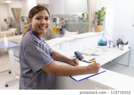 Mature adult nurse writing on clipboard with orange pen at hospital ward desk, with infusion pumps Mature adult nurse writing on clipboard with orange pen at hospital ward desk, with infusion pumps 128738502