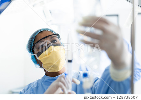 Female healthcare worker adjusting IV bag and tubing in clinical setting, with gloves Female healthcare worker adjusting IV bag and tubing in clinical setting, with gloves 128738507
