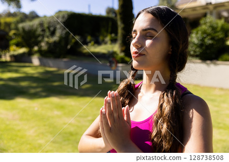 Woman meditating in sunny backyard garden wearing pink athletic tank top, copy space Woman meditating in sunny backyard garden wearing pink athletic tank top, copy space 128738508