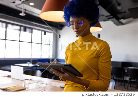 African American young adult woman using stylus on tablet at table in co-working space, copy space 128738529