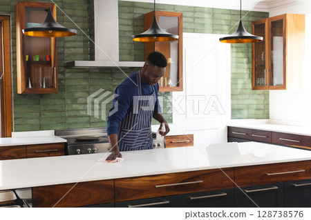 African American man cleaning quartz countertop in modern kitchen, with spray bottle and cloth African American man cleaning quartz countertop in modern kitchen, with spray bottle and cloth 128738576