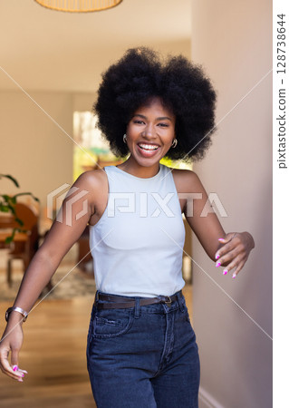 African American woman walking toward camera in hallway, overlooking wooden table and plant 128738644