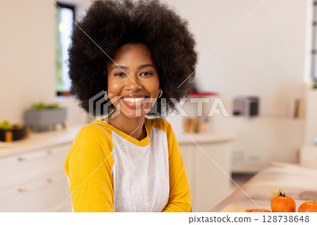 African American woman leaning on kitchen island, smiling and showcasing orange tomatoes in kitchen 128738648