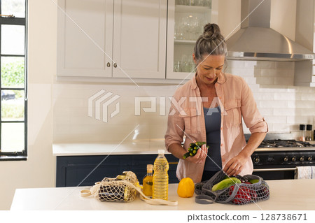 Sorting senior woman arranging vegetables at kitchen island, with mesh produce bags, copy space Sorting senior woman arranging vegetables at kitchen island, with mesh produce bags, copy space 128738671