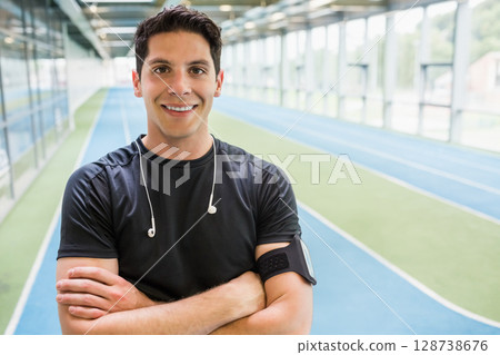 Man standing on blue running track lanes at sports complex, wearing fitness armband and earphones 128738676