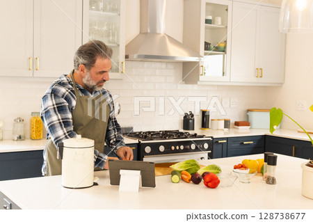 Man chopping vegetables on cutting board in modern kitchen, with tablet, fresh produce, copy space 128738677