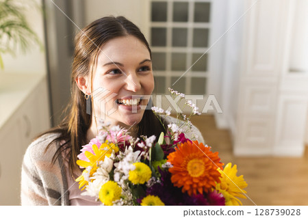 Woman smiling and holding colorful bouquet in home hallway, with built-in cabinet and plant Woman smiling and holding colorful bouquet in home hallway, with built-in cabinet and plant 128739028