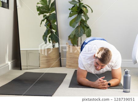 Man holding forearm plank on yoga mat at home, with mirror plant water bottle, copy space Man holding forearm plank on yoga mat at home, with mirror plant water bottle, copy space 128739051