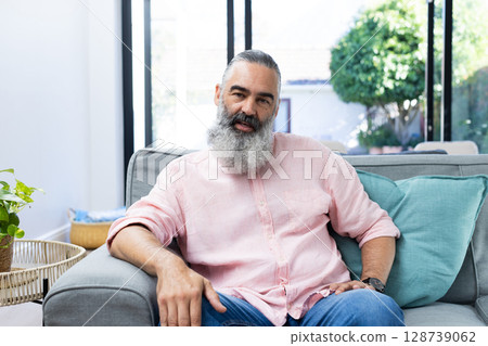 Man sitting on gray sofa at home, with wicker table, potted plant and sliding glass door 128739062