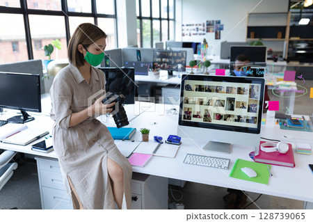 Diverse coworkers inspecting DSLR camera at open office desk, with computer thumbnails, copy space 128739065