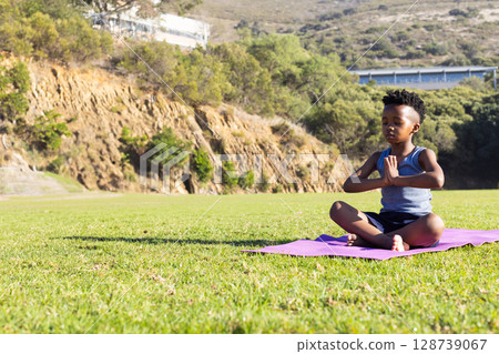 African American boy meditating on pink yoga mat in public park, finding calm focus, copy space 128739067